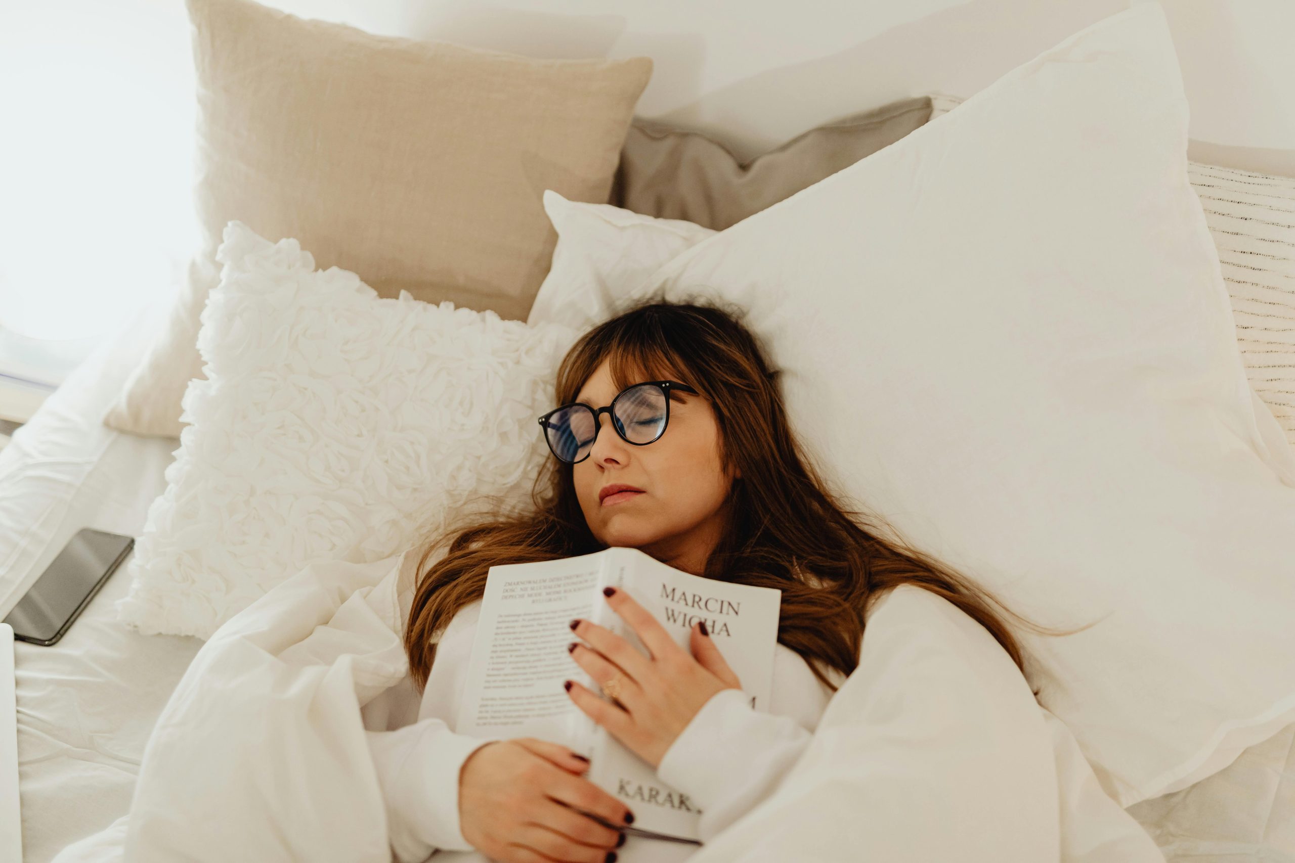 A woman resting with a book in bed, showcasing a cozy and serene atmosphere.