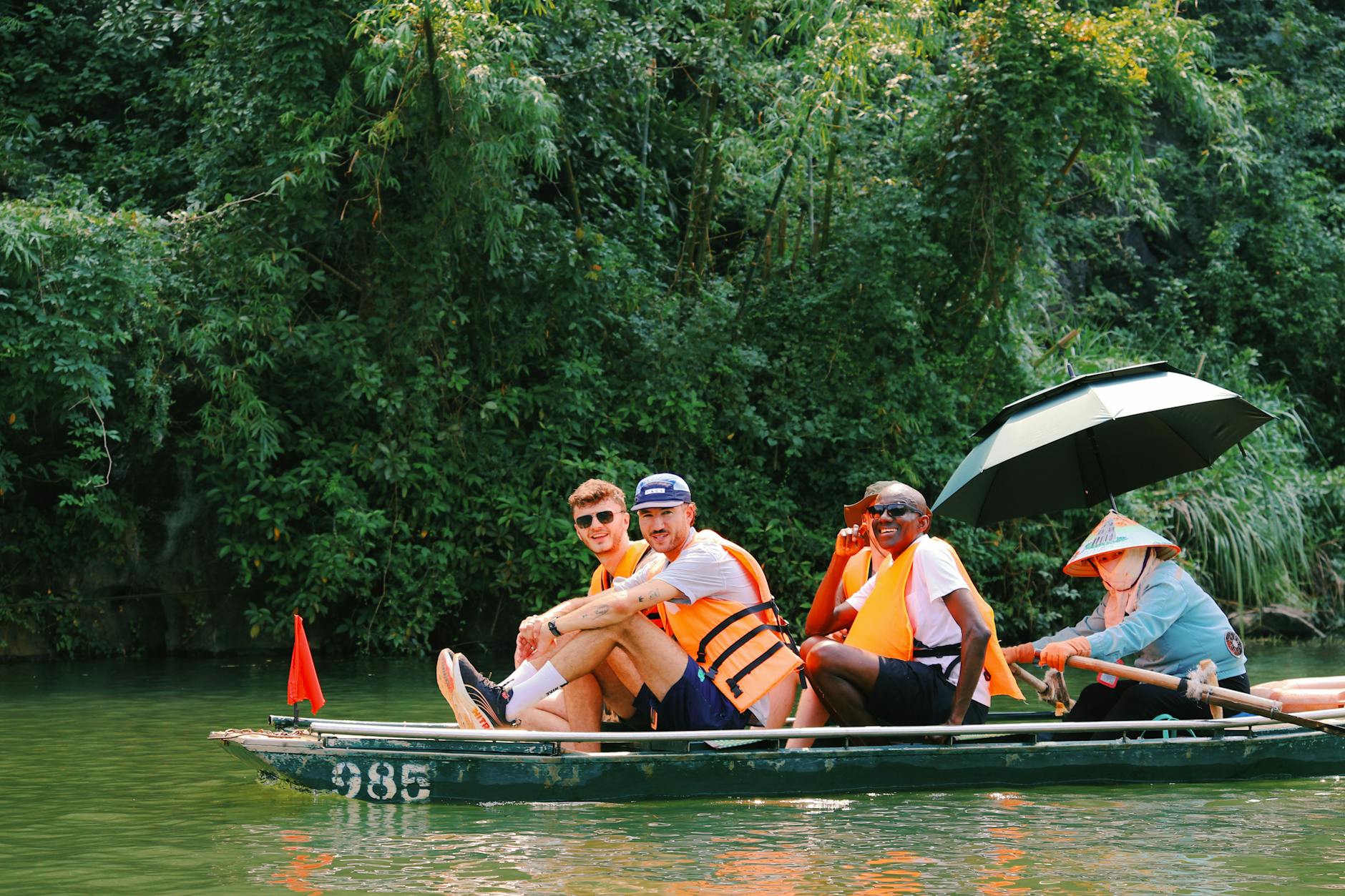 Group enjoying a boat ride in lush Hoa Lư, Vietnam, amidst vibrant greenery.