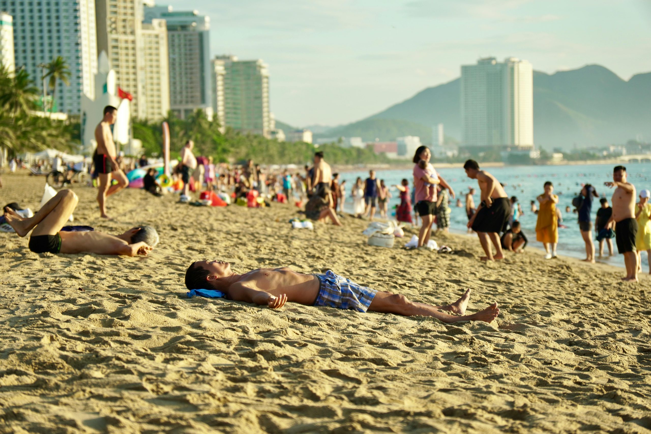 A bustling beach in Nha Trang with people sunbathing and enjoying a sunny day by the sea.