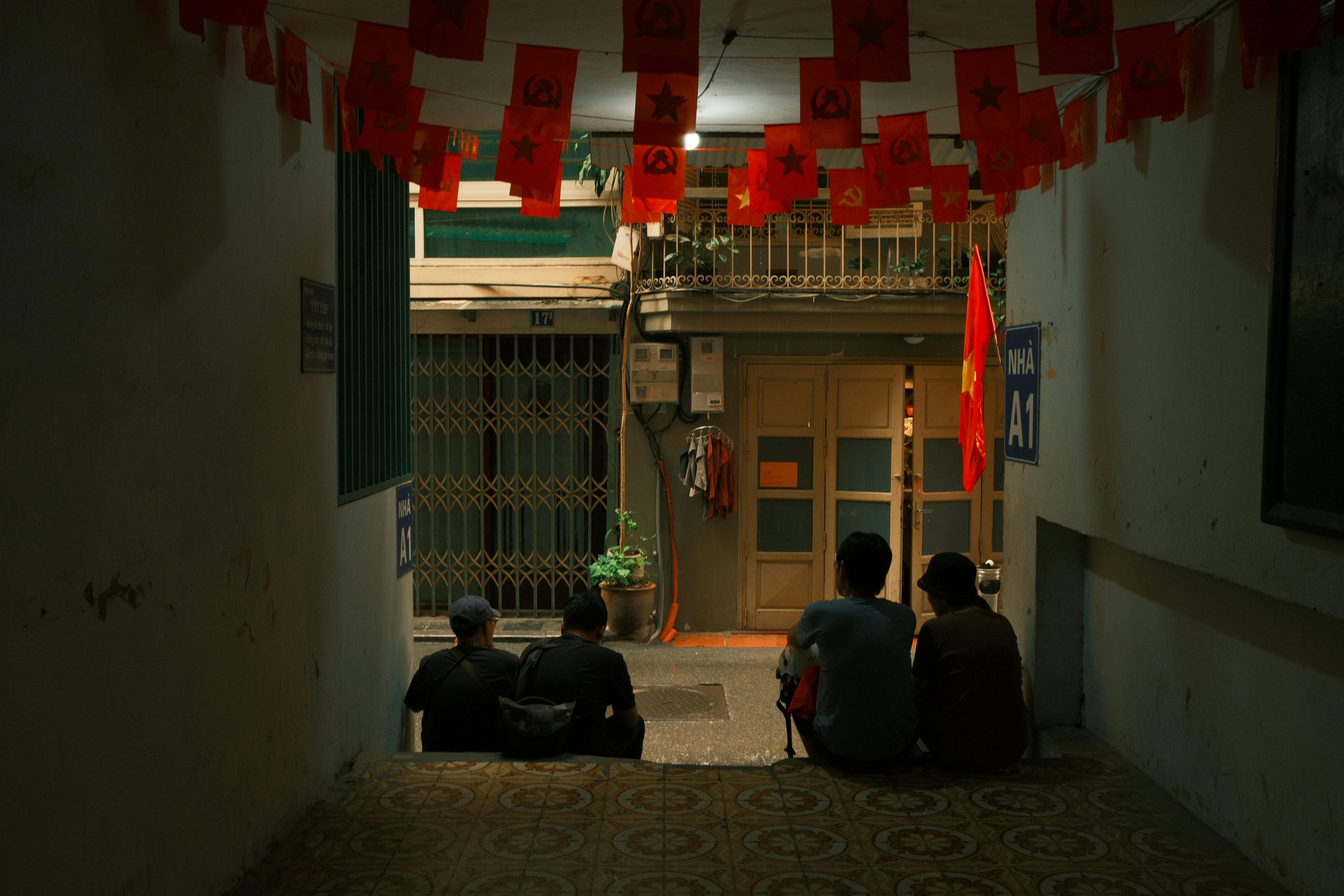 A peaceful evening scene with people sitting under flags in an Osaka alleyway.