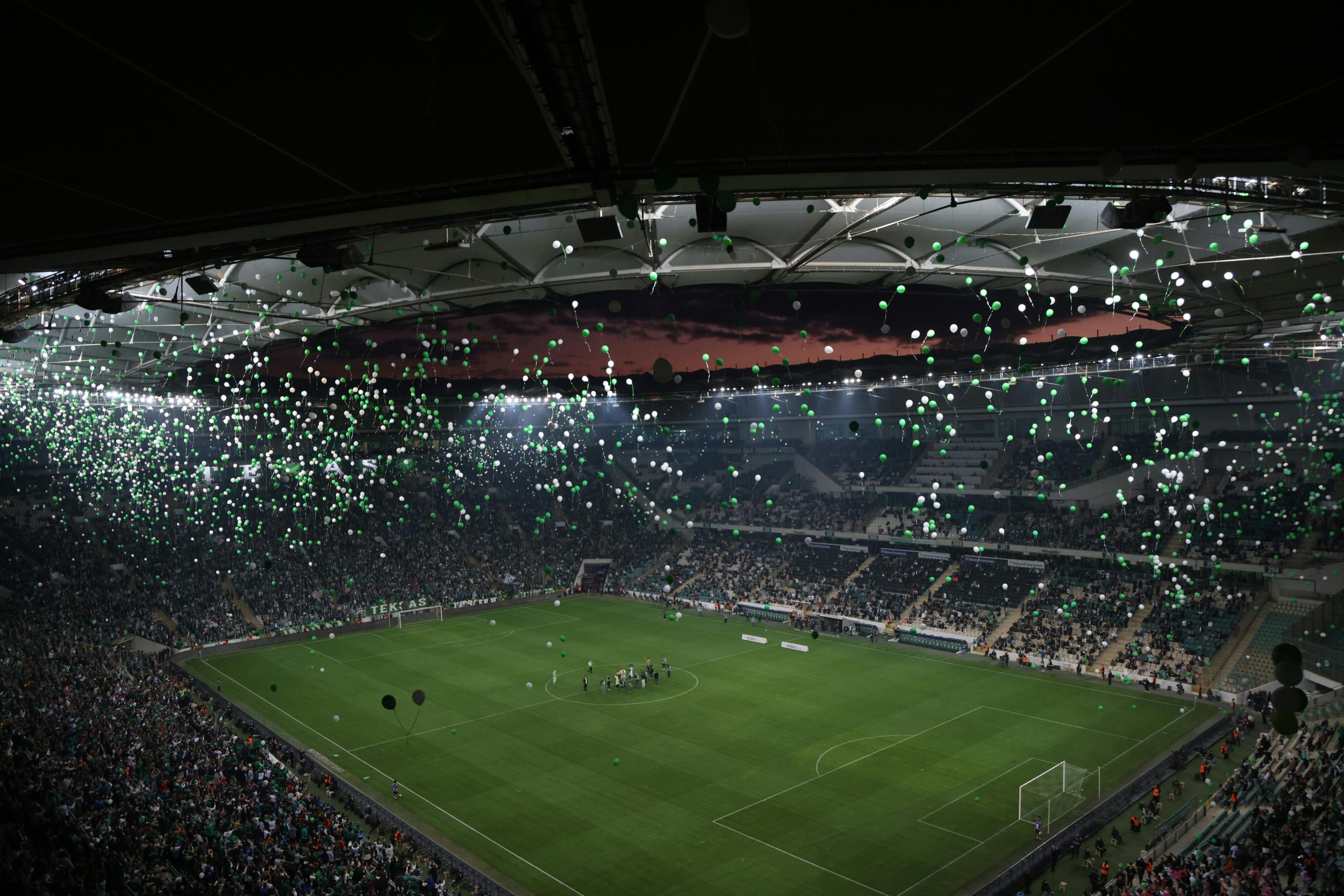 A crowded stadium at twilight with balloons filling the sky, creating a festive atmosphere.