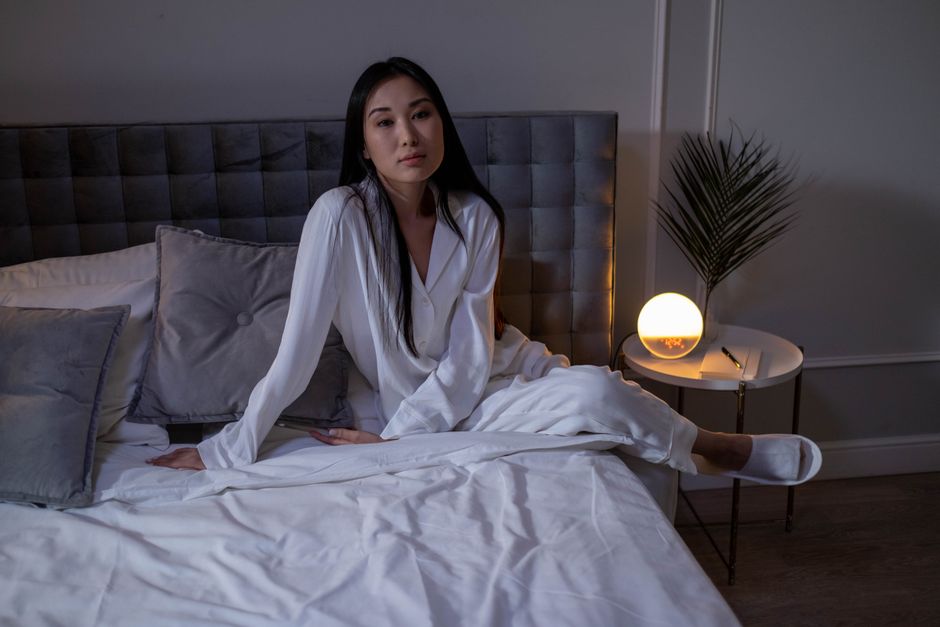 A woman in white sleepwear sitting on a modern bed in a cozy bedroom.